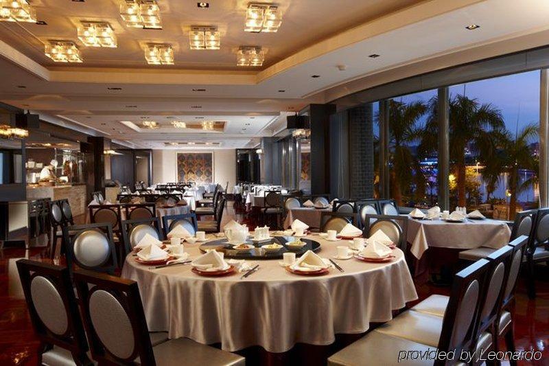 Ambassador Hotel Kaohsiung Exterior photo The photo depicts an elegant restaurant interior. It features round tables, each covered with white tablecloths and set with dishes and utensils, suggesting a formal dining experience. The restaurant has a modern and sophisticated design, with a well