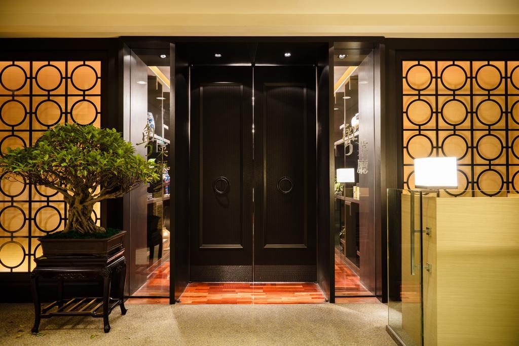 Ambassador Hotel Kaohsiung Exterior photo The photo shows an elegant entrance area featuring a set of large black double doors, which appear to be a main entryway. The walls surrounding the doors have a decorative design with circular patterns. On one side, there is a small tree in a planter