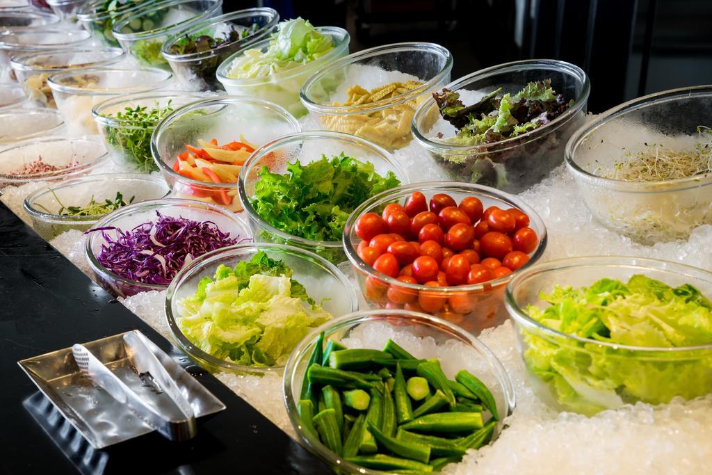 Ambassador Hotel Kaohsiung Exterior photo The photo displays a vibrant array of fresh vegetables and greens arranged in clear bowls on a bed of ice. The selection includes various leafy greens, chopped vegetables, and colorful ingredients. There are items like cherry tomatoes, purple cabbage