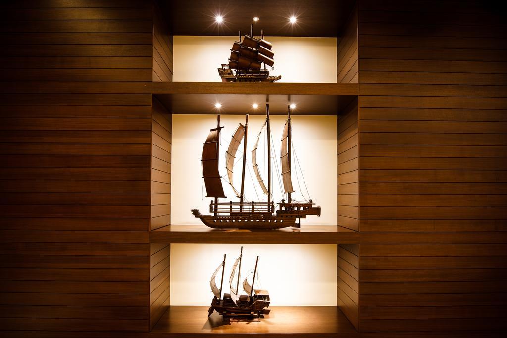 Ambassador Hotel Kaohsiung Exterior photo The photo displays three model ships arranged on shelves with a warm wood background. Each ship has distinct features and varying sizes, showcasing different designs. The top ship has a traditional Asian style with sails, the middle ship appears to b