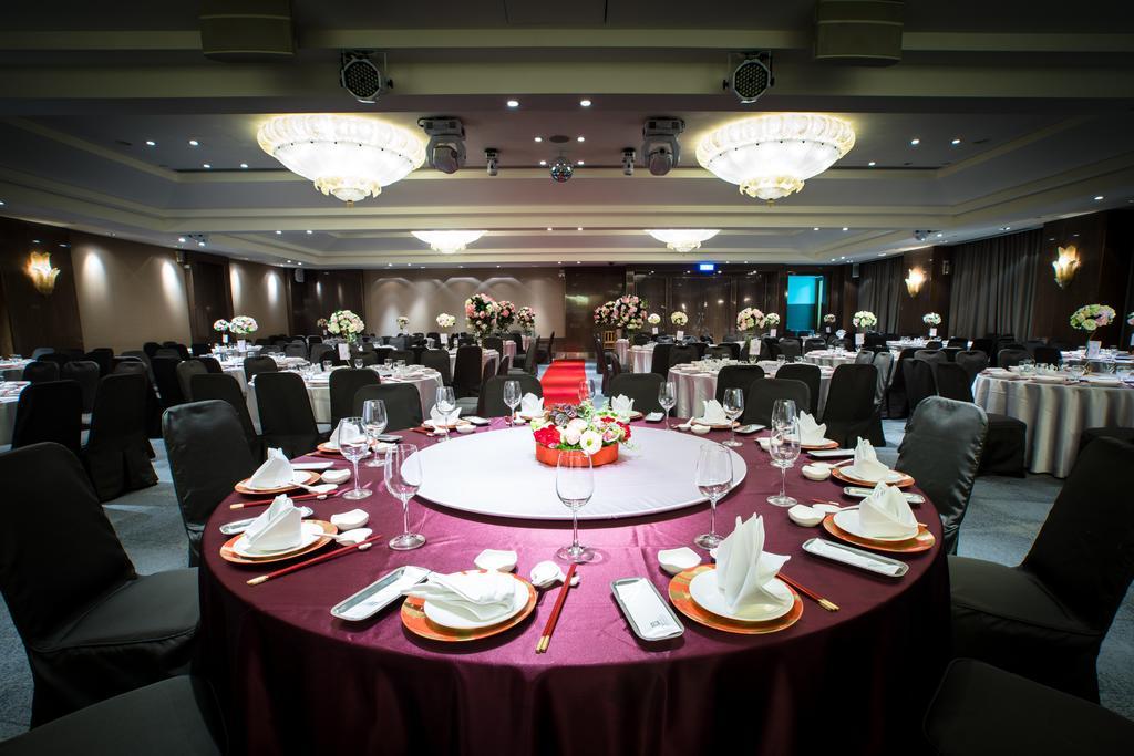 Ambassador Hotel Kaohsiung Exterior photo The photo depicts an elegantly set dining area for an event. 

In the foreground, there is a circular table covered with a dark red tablecloth, featuring a centerpiece of flowers in vibrant colors. The table is equipped with white plates, polished cu