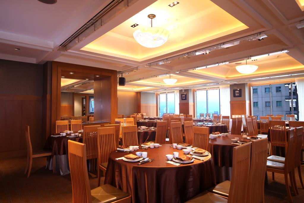 Ambassador Hotel Kaohsiung Exterior photo The photo shows the interior of a restaurant. It features several round tables covered with brown tablecloths, each set with plates and utensils. The room is well-lit with overhead lighting, and large windows allow natural light to enter, providing a