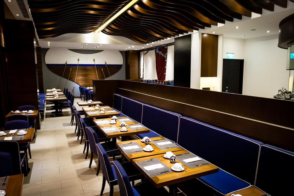 Ambassador Hotel Kaohsiung Exterior photo The photo shows the interior of a modern restaurant. The design features a combination of wooden and blue elements, with sleek lines and a stylish ceiling design. There are several tables set up, each with white plates and utensils. The seating inclu