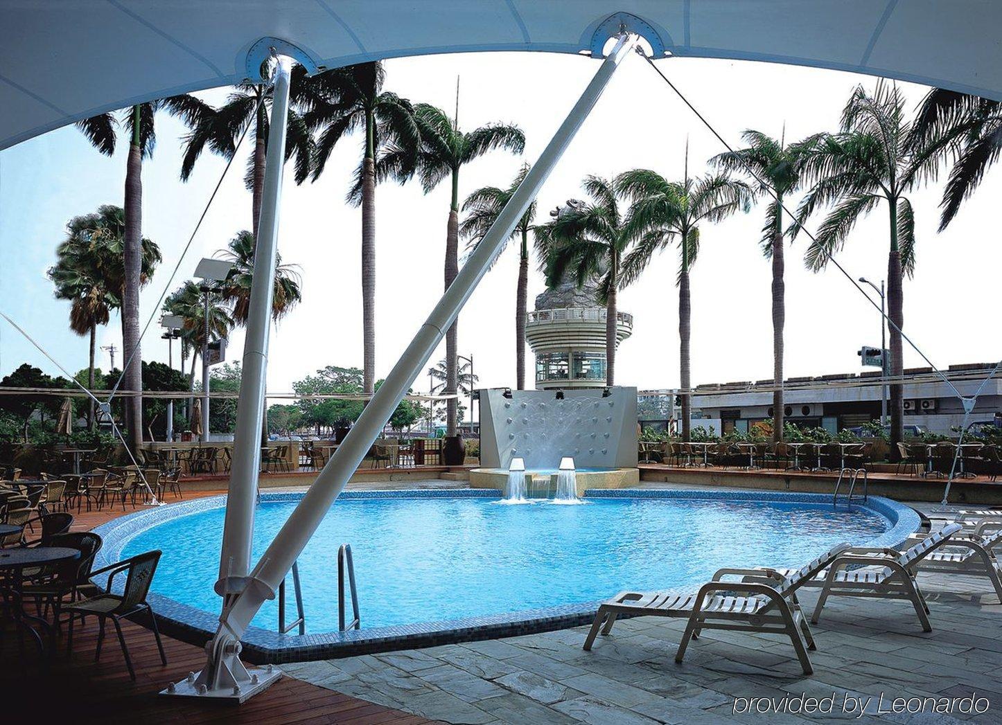 Ambassador Hotel Kaohsiung Exterior photo The photo shows a swimming pool area surrounded by tall palm trees. The pool has a clear blue water and features a waterfall-like structure. There are lounge chairs positioned around the pool, suggesting a relaxing atmosphere. A covered area provides