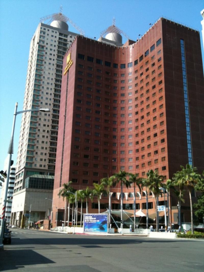 Ambassador Hotel Kaohsiung Exterior photo The photo shows a tall building made of red brick with many windows. It has a curved shape and is likely a hotel or office building. In front of the building, there are palm trees, suggesting a warm climate. To the left, there appears to be another t