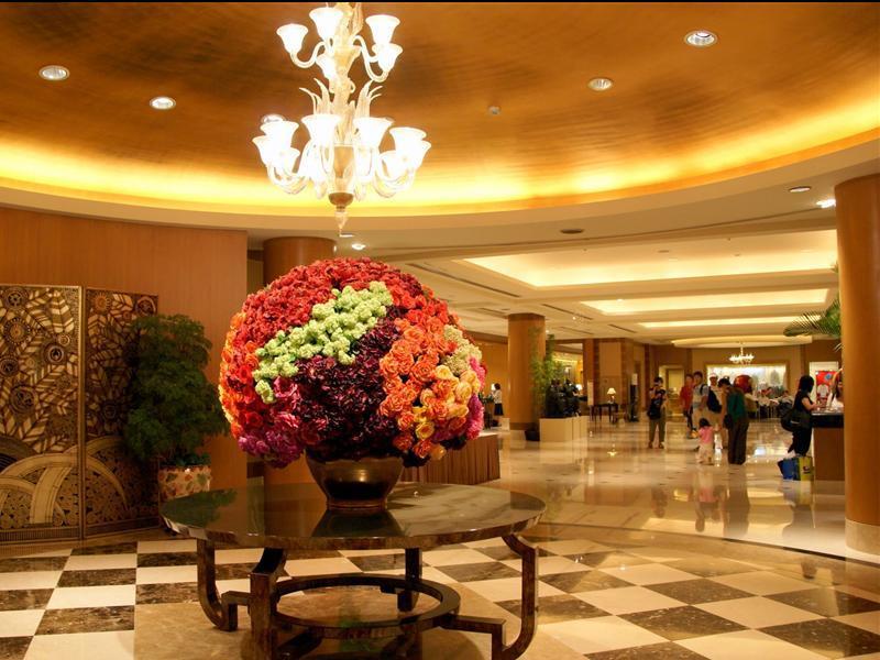 Ambassador Hotel Kaohsiung Exterior photo The photo shows the interior of a spacious lobby area, characterized by elegant design elements. In the center, there is a large round floral arrangement made up of vibrant flowers in various colors, displayed in a decorative vase on a dark, round ta