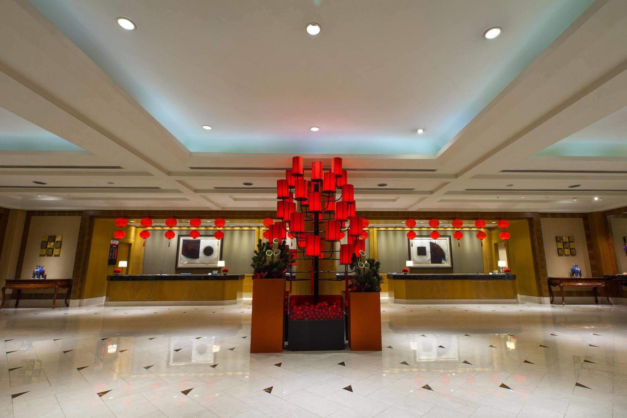 Ambassador Hotel Kaohsiung Exterior photo The photo depicts the interior of a hotel lobby. The area is well-lit and features elegant design elements. In the center, there is a striking installation of red lanterns, which adds a festive touch to the space. The lobby has a polished marble floo
