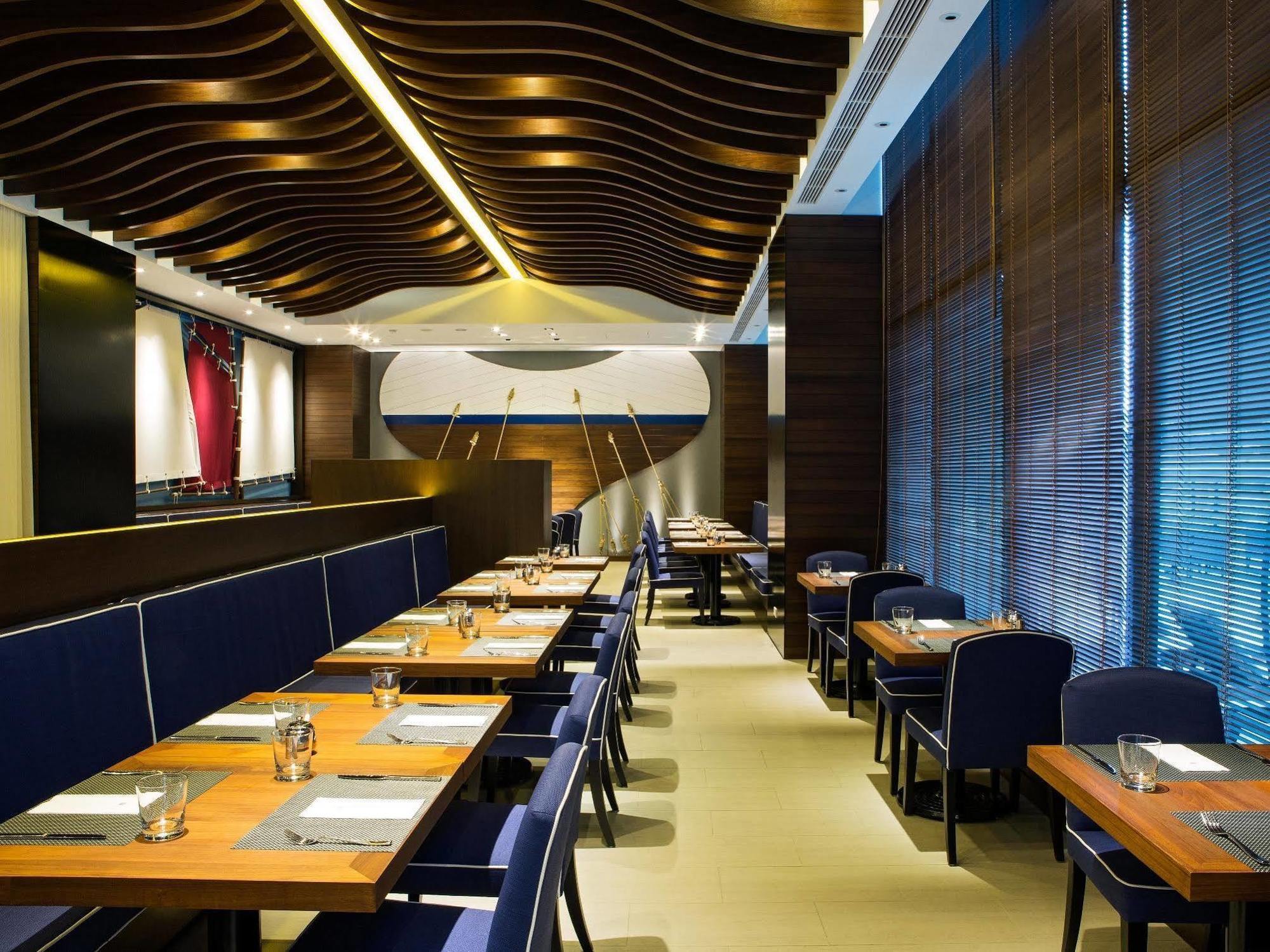 Ambassador Hotel Kaohsiung Exterior photo The photo shows the interior of a modern restaurant. It features wooden flooring and stylish seating arrangements with tables. The tables are set with menus, cutlery, and glasses, indicating a dining setup. The walls are adorned with contemporary des