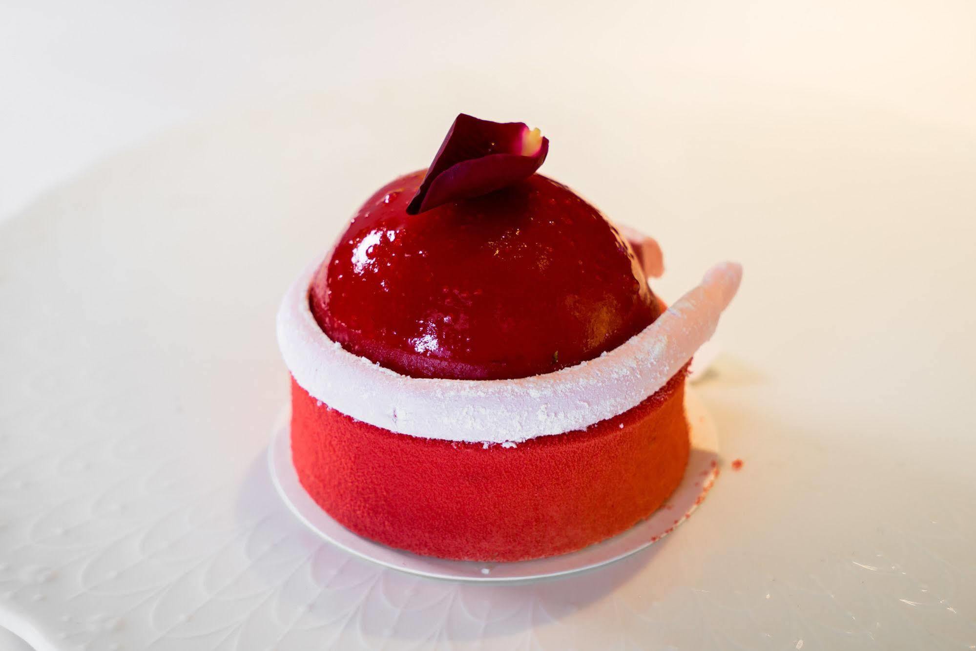 Ambassador Hotel Kaohsiung Exterior photo The photo shows a beautifully crafted dessert that appears to be a mousse or cake. It has a glossy red coating, shaped like a dome on top, with a small decorative rose petal placed on it. The base of the dessert features a gradient of colors, transit