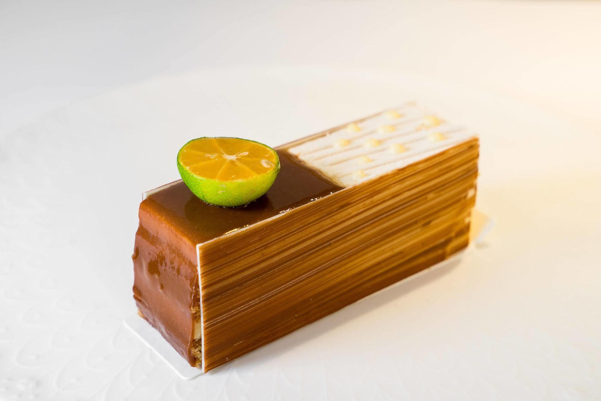 Ambassador Hotel Kaohsiung Exterior photo The photo shows a dessert that is shaped like a rectangular block or loaf. It features a glossy, golden-brown exterior, likely made with layers of chocolate or caramel. Atop the dessert, there is a halved lime slice, adding a pop of color and suggest