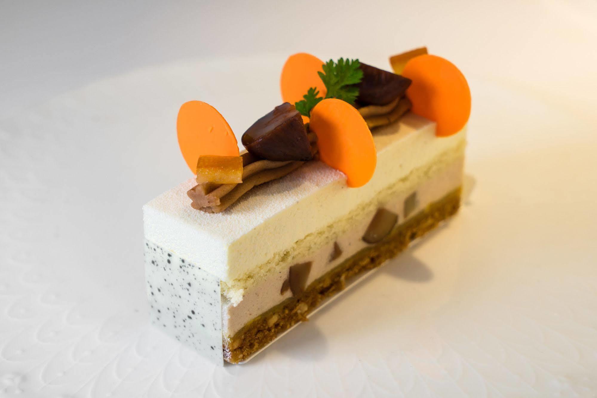 Ambassador Hotel Kaohsiung Exterior photo The photo features a dessert that appears to be a modern, layered cake or mousse. It has a rectangular shape and is composed of several distinct layers. The top layer is a light-colored mousse or cream, decorated with vibrant orange, circular element