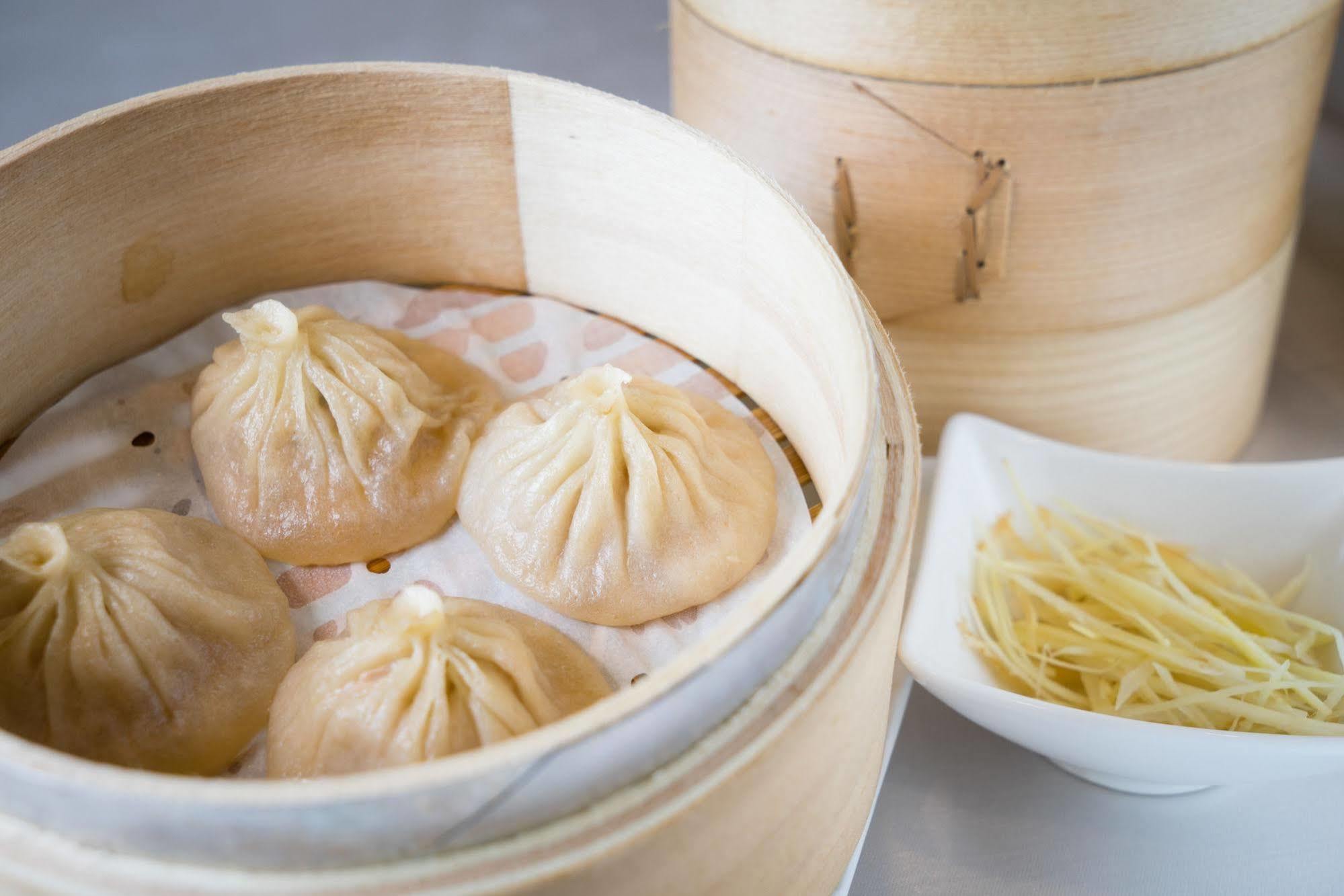 Ambassador Hotel Kaohsiung Exterior photo The photo shows a bamboo steamer containing several dumplings, known as xiaolongbao, which are soup dumplings traditionally filled with meat and broth. The dumplings are arranged neatly on a layer of parchment paper inside the steamer. Next to the st