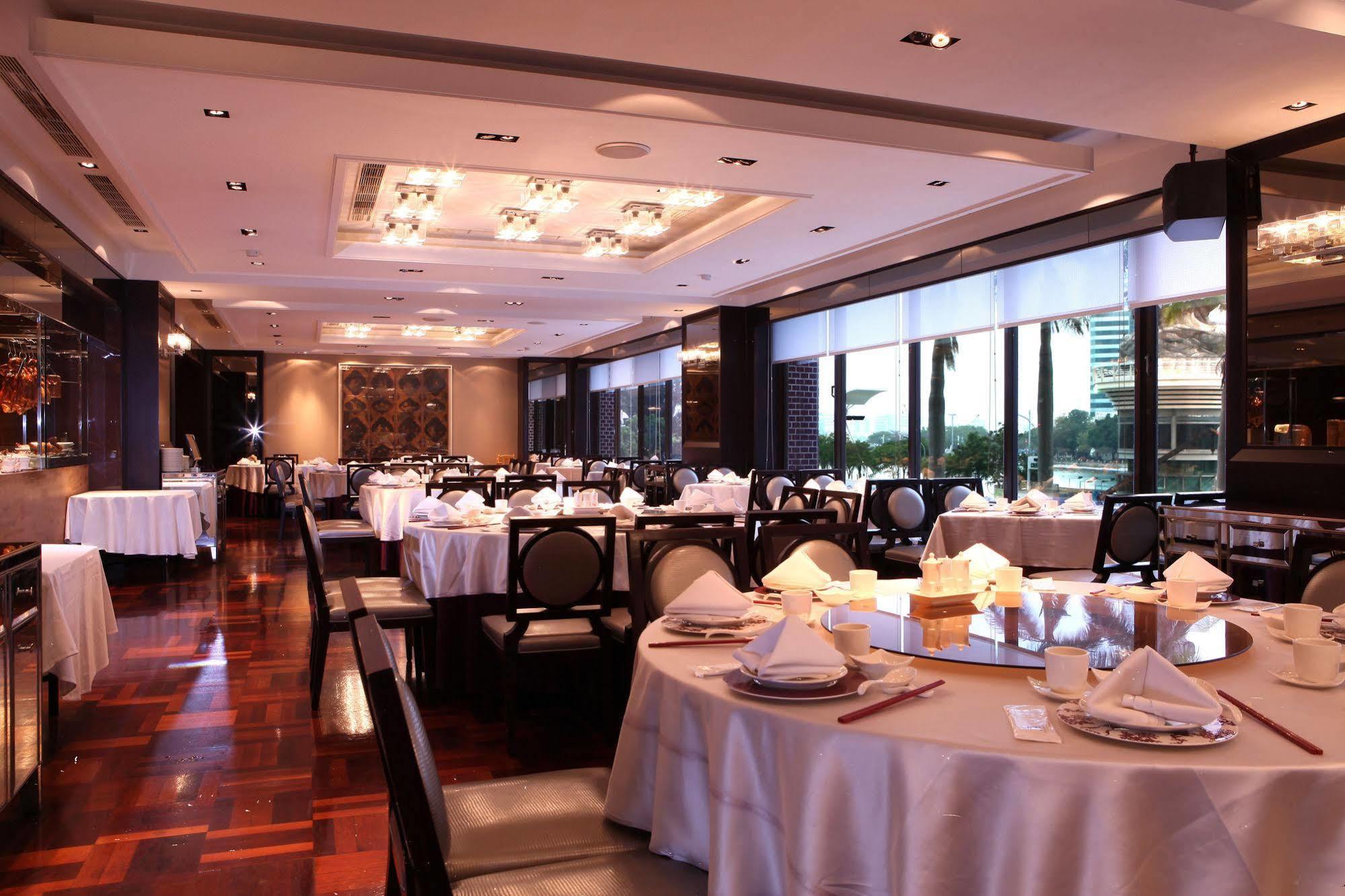 Ambassador Hotel Kaohsiung Exterior photo The photo shows an elegant restaurant interior. It features neatly arranged tables with white tablecloths and dining settings, including plates, cutlery, and folded napkins. The space is well-lit with ambient lighting and large windows that likely pr