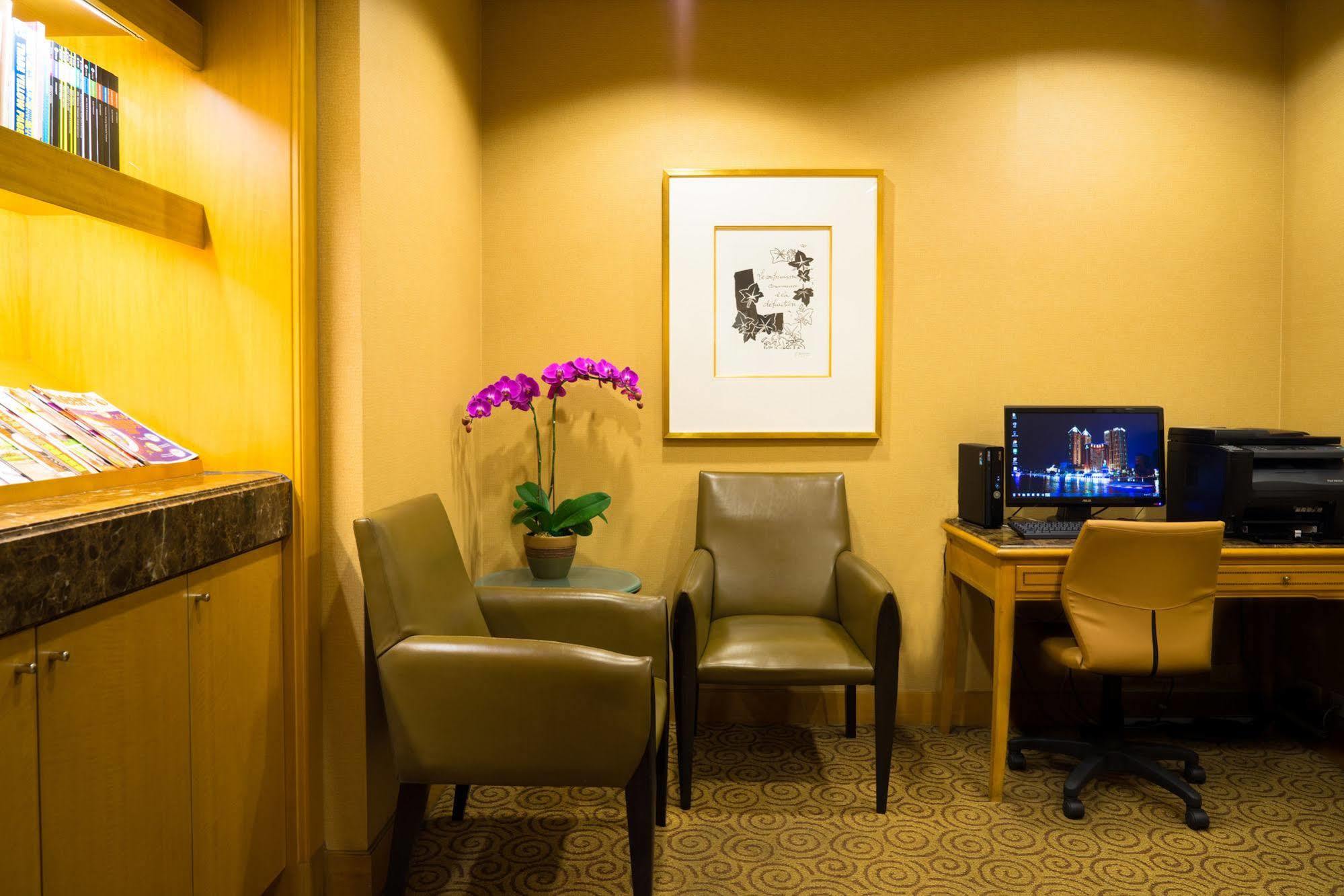 Ambassador Hotel Kaohsiung Exterior photo The photo shows a cozy corner of a room, which appears to be a waiting or lounge area. There are two stylish chairs positioned near a small table. A potted plant with purple flowers adds a touch of color and freshness to the space. On the wall, there