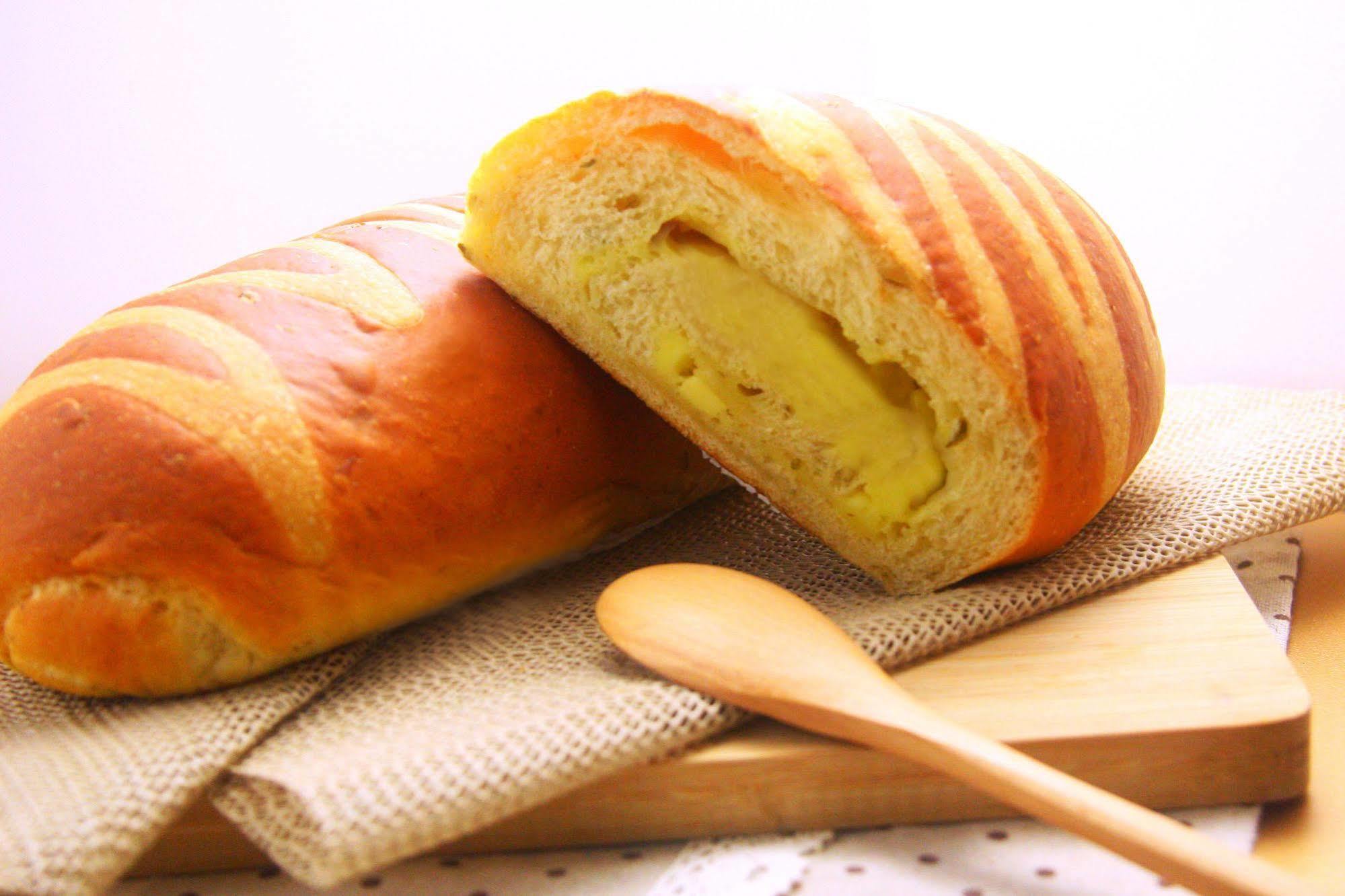 Ambassador Hotel Kaohsiung Exterior photo The photo shows a loaf of bread that has a golden-brown crust with striped patterns on its surface. One loaf is partially sliced open, revealing a soft, yellow filling inside, which suggests that it might be flavored or sweetened. The bread is placed