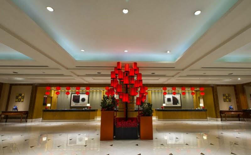 Ambassador Hotel Kaohsiung Exterior photo The photo shows a hotel lobby with a modern and elegant design. In the center, there is a striking red display, likely made up of lanterns or decorative elements, creating a vibrant focal point. The lobby features a polished floor that reflects the l