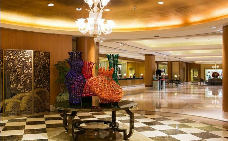 Ambassador Hotel Kaohsiung Exterior photo The image shows a spacious and elegantly designed lobby area. In the center, there are several large, artistic vases made of colorful materials, including shades of purple, orange, and green. These vases are displayed on a black table, contrasting wi